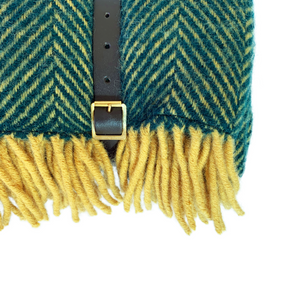 Close up of the buckle on the leather carry strap of a rolled up green herringbone wool picnic blanket