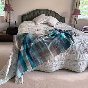Blue, green, white and brown check merino wool throw on a double bed