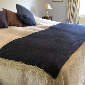 Navy blue herringbone wool throw folded over the base of a double bed