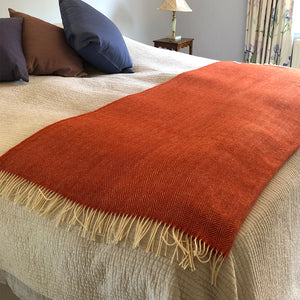 Orange herringbone wool interior throw folded over the bottom of a double bed