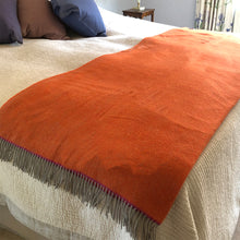 Orange wool throw folded over the base of a bed